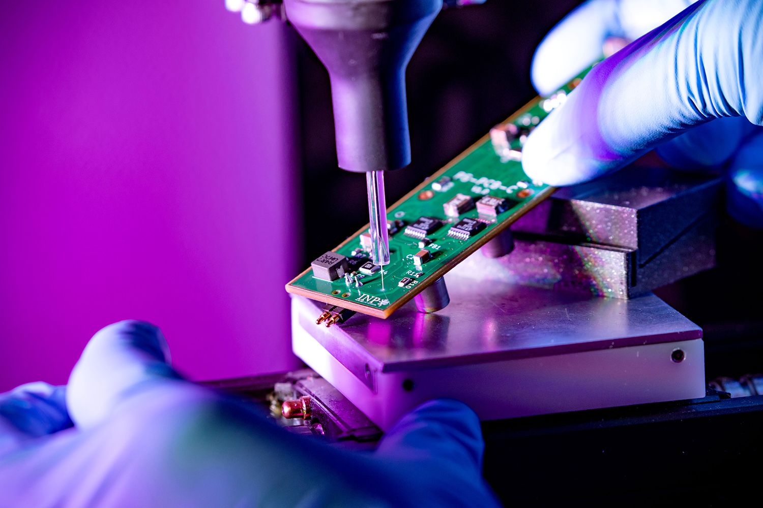 Plasmadüse bearbeitet eine Leiterplatte im Labor; eine gloved Hand fixiert das Bauteil während der präzisen Oberflächenmodifikation.