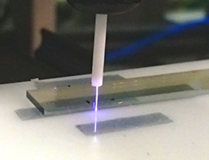 Atmosphärischer Plasmastrahl trifft auf eine längliche Probenoberfläche, um deren optische Eigenschaften gezielt zu verändern.
