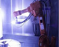 Plasmasprayanlage mit Industrieroboter, der eine Plasmaquelle zur Beschichtung oder Modifizierung einer Oberfläche in einer abgeschirmten Anlage führt.