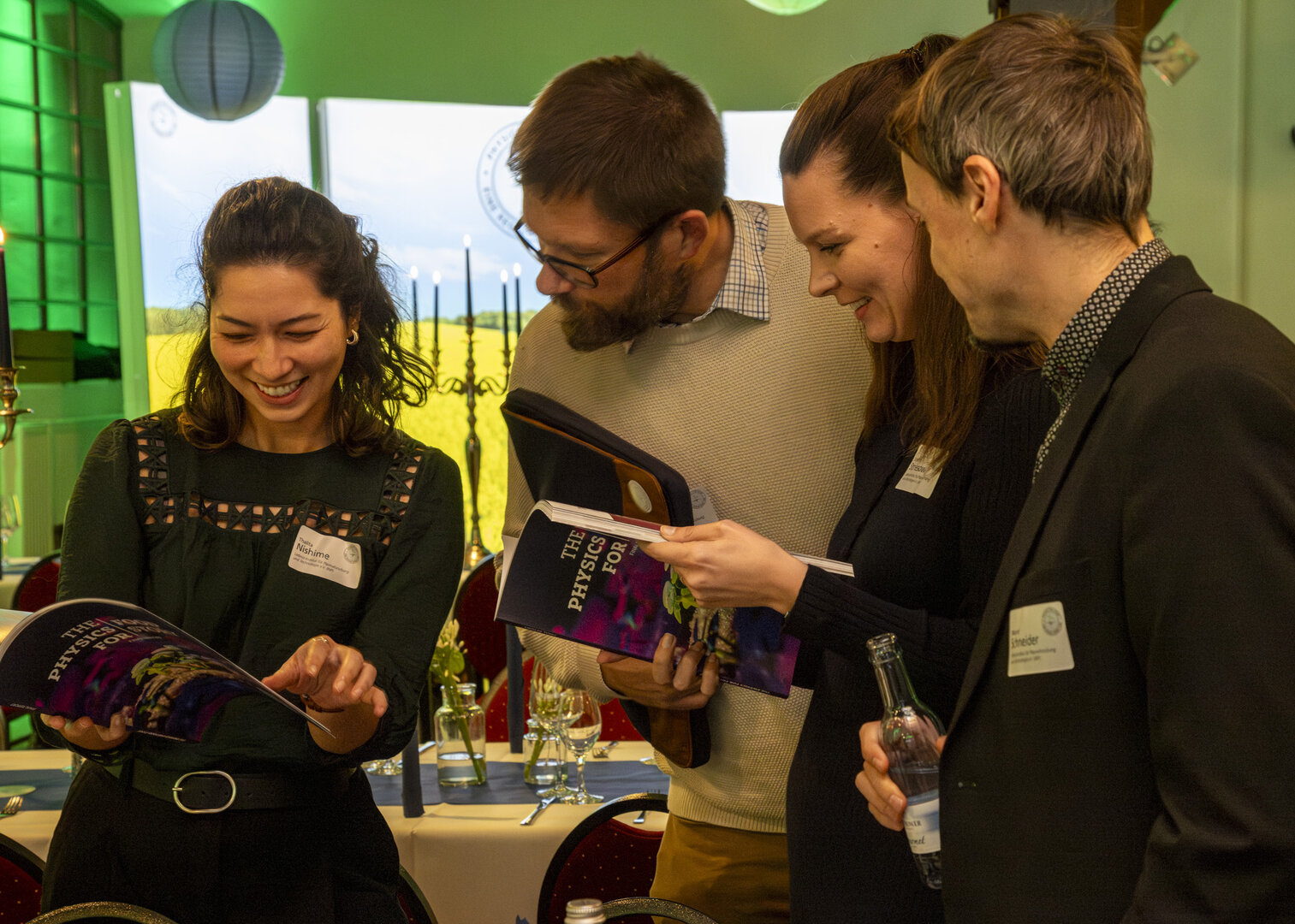 Vier Teilnehmende der Abschlussveranstaltung betrachten gemeinsam eine Broschüre des Projekts „Physics for Food“.