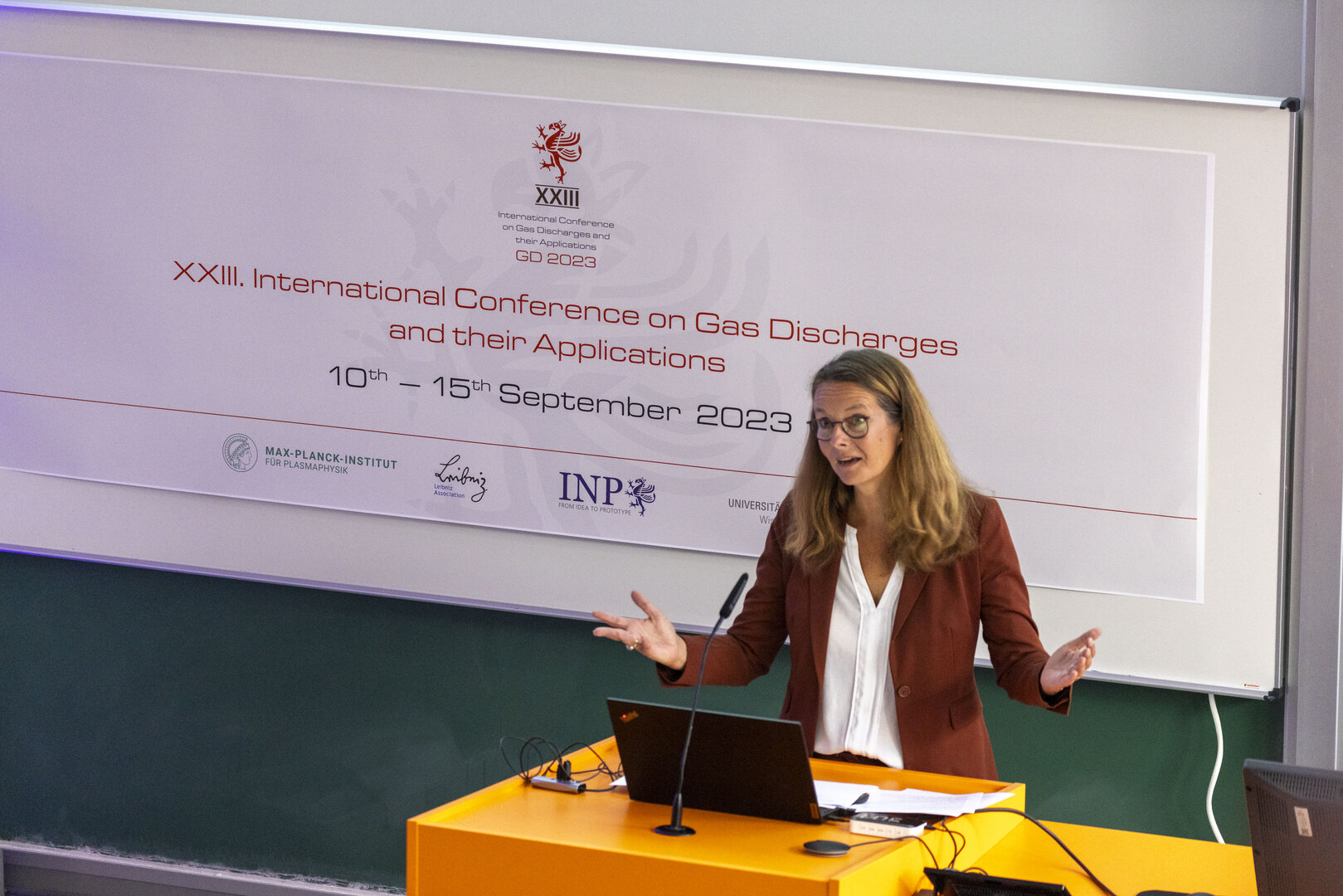 Bettina Martin eröffnet die GD2023-Konferenz an einem Rednerpult vor Konferenzbanner in einem Hörsaal in Greifswald.
