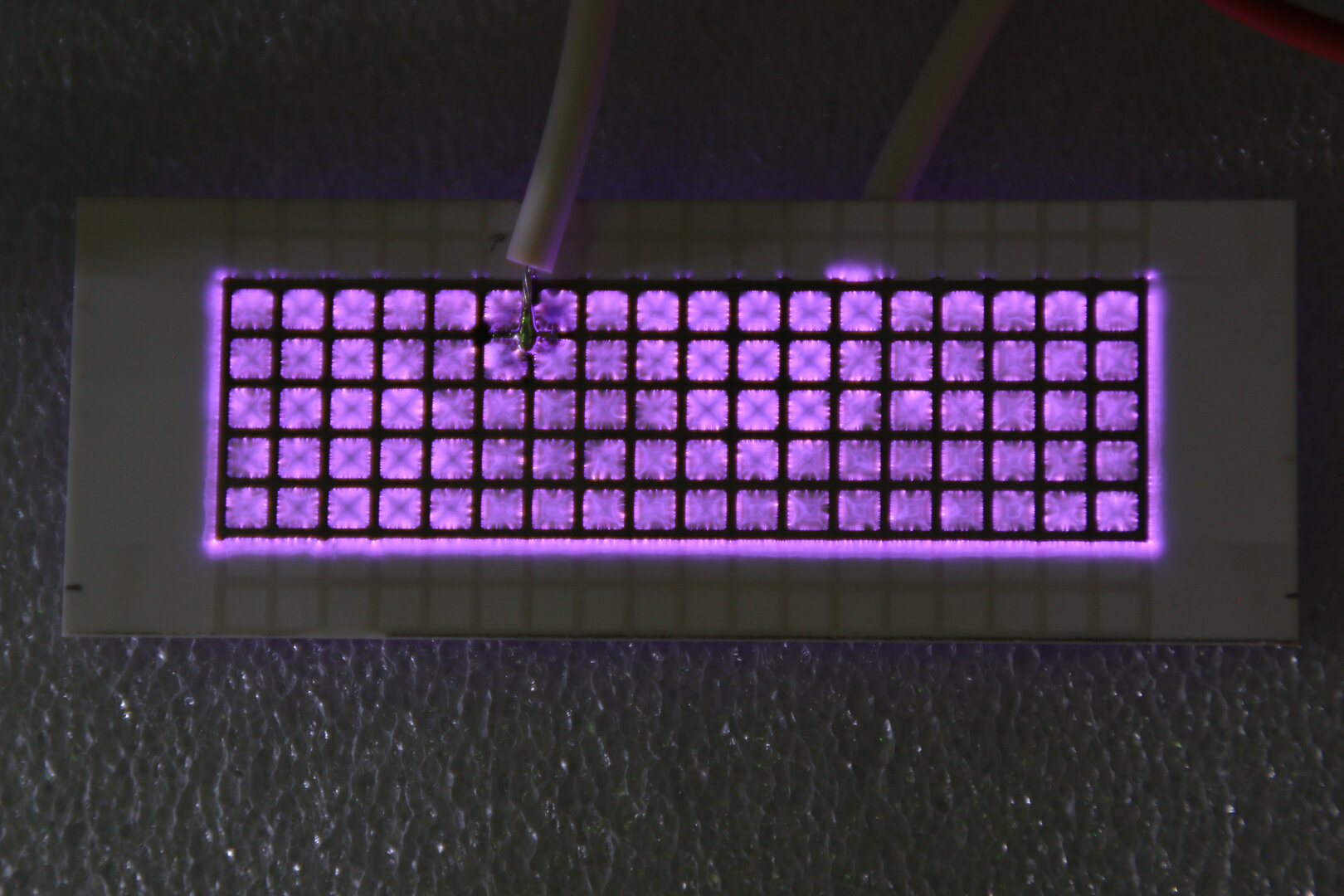 Elektrodenmodul mit gleichmäßig angeordneten dielektrisch behinderten Entladungen in violettem Plasma­licht.