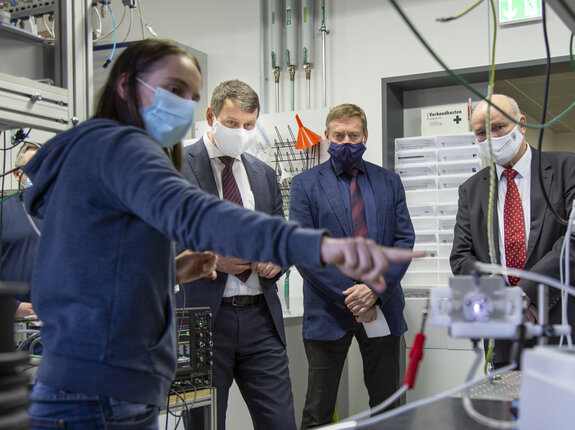 Dr. Katja Zocher demonstriert im INP-Labor eine Anwendung von kaltem Atmosphärendruckplasma; Michael Sack, Klaus-Dieter Weltmann und Egbert Liskow beobachten die Erklärung, alle tragen Masken.