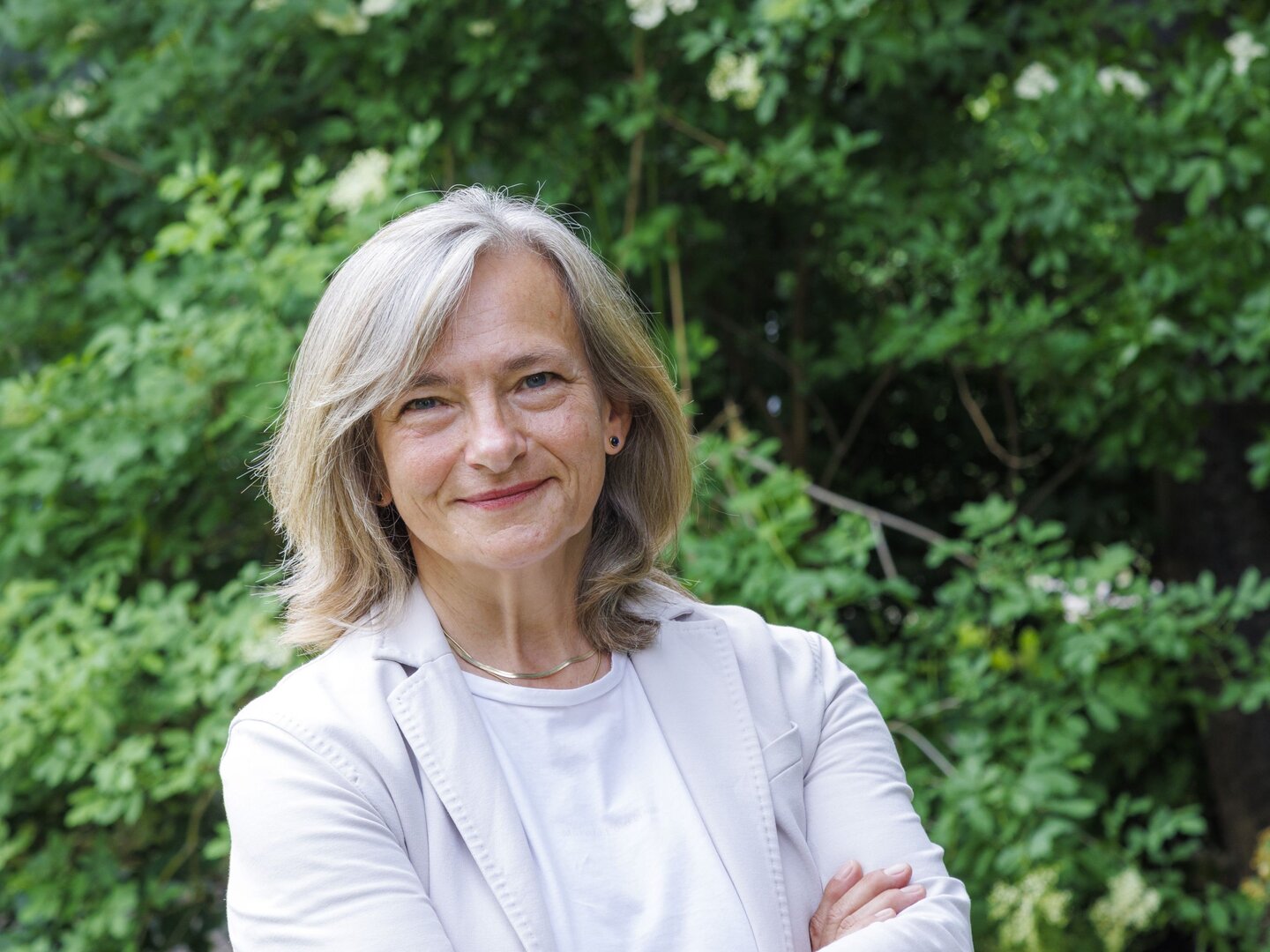 Dr. Helga Andree im Porträt vor grüner Vegetation.