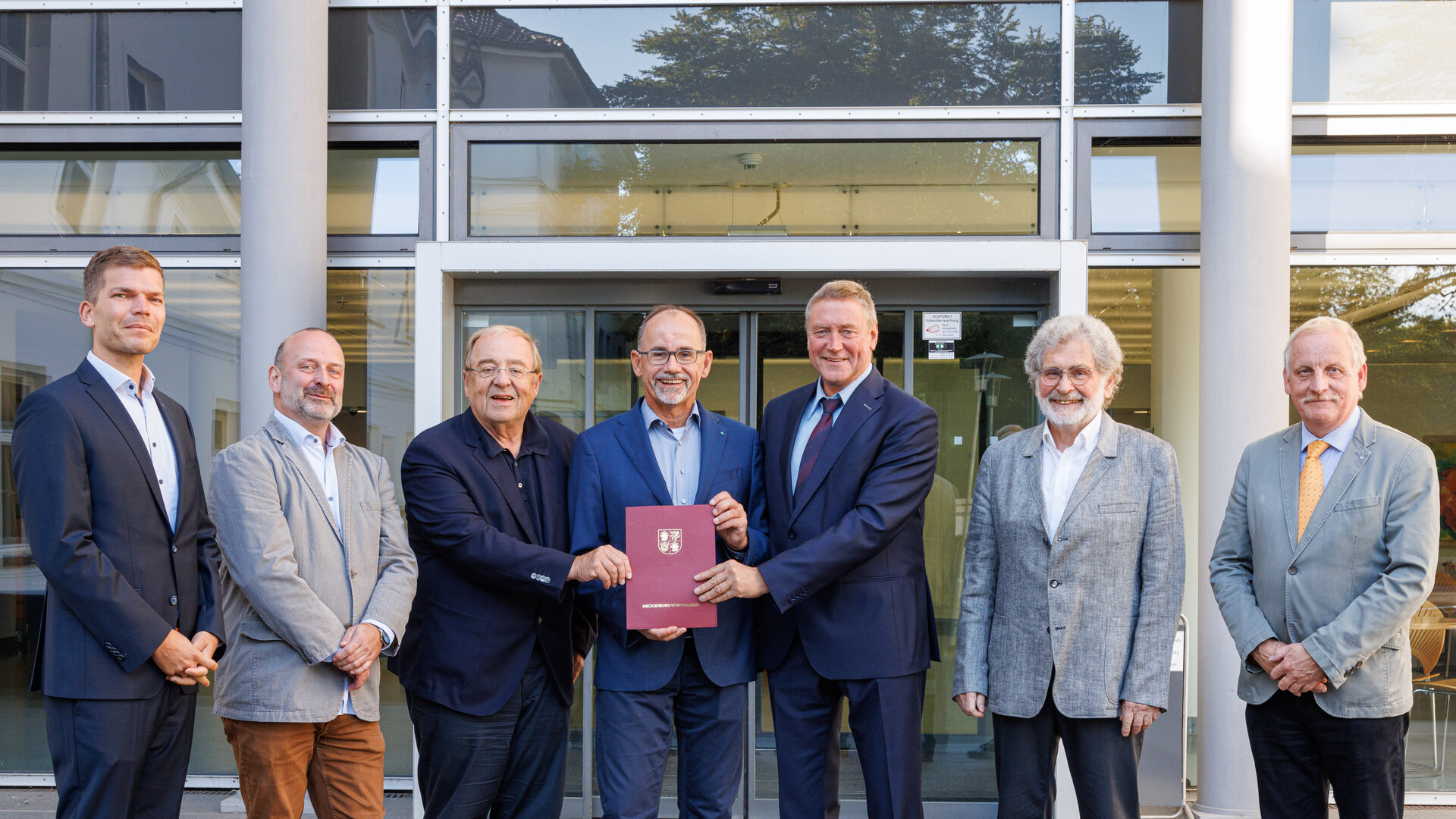 Wirtschaftsminister Dr. Wolfgang Blank überreicht vor dem KDK-Gebäude einen Förderbescheid an Prof. Klaus-Dieter Weltmann, begleitet von Prof. Dr. med. Wolfgang Motz und weiteren Beteiligten.