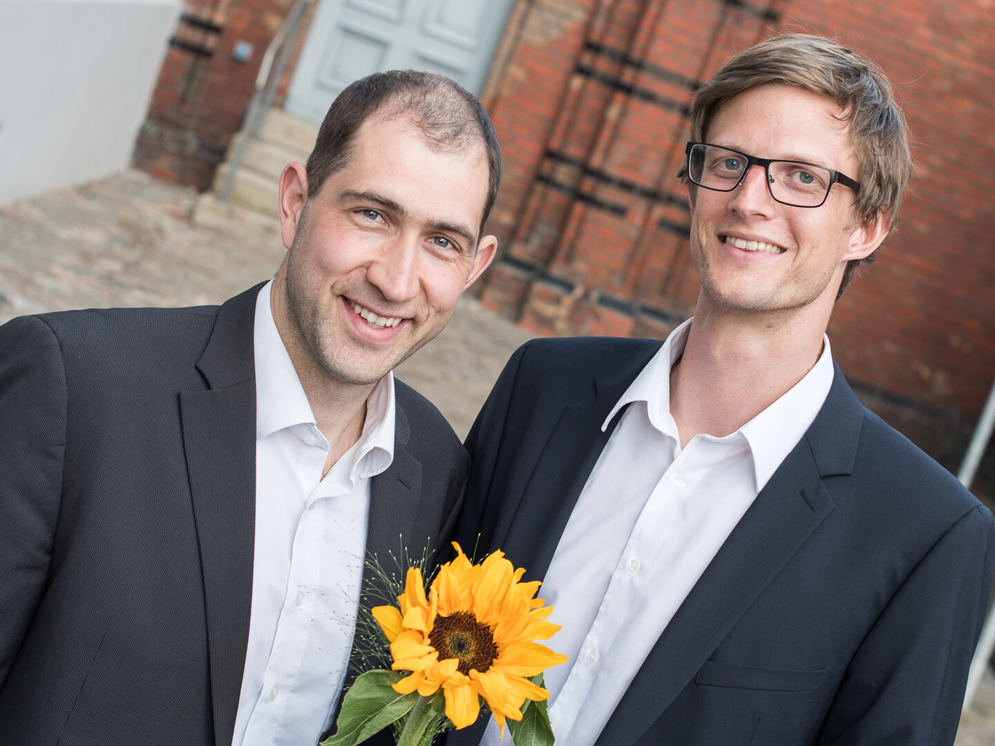 Dr. Jörn Winter und Dr. Ansgar Schmidt-Bleker stehen im Außenbereich und halten eine Sonnenblume anlässlich ihrer Auszeichnung im UNIQUE-Ideenwettbewerb.