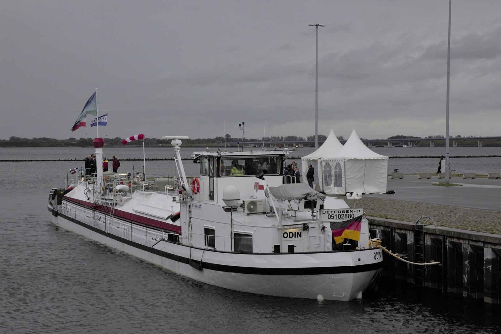 Das Ammoniak-Bunkerschiff „Odin“ liegt im Hafen von Stralsund an der Kaimauer; einige Personen stehen an Deck, daneben weiße Messezelte.