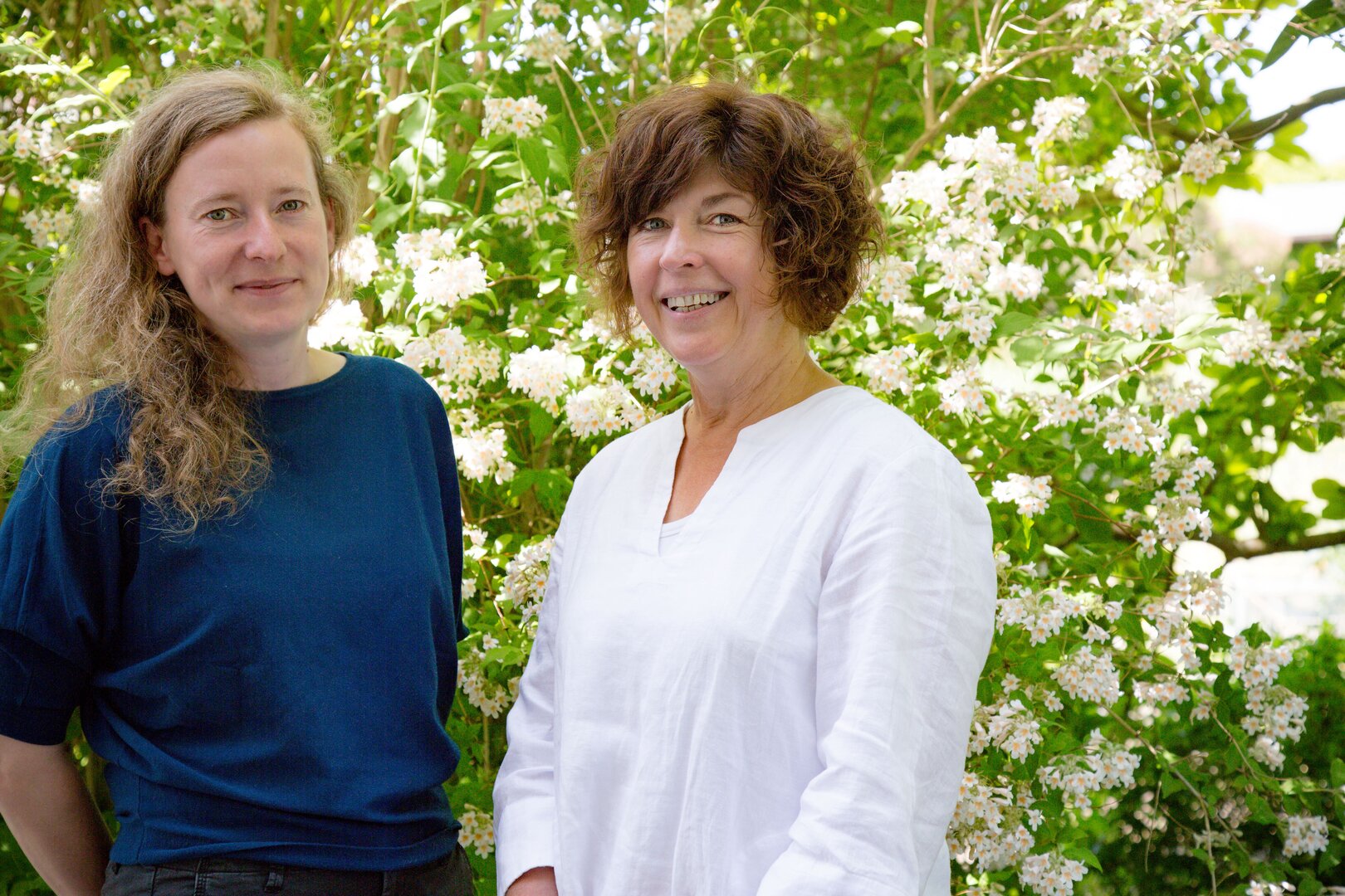 Dr. Henrike Brust (links, INP) und Prof. Christine Stöhr (Universität Greifswald) stehen vor blühenden Sträuchern.