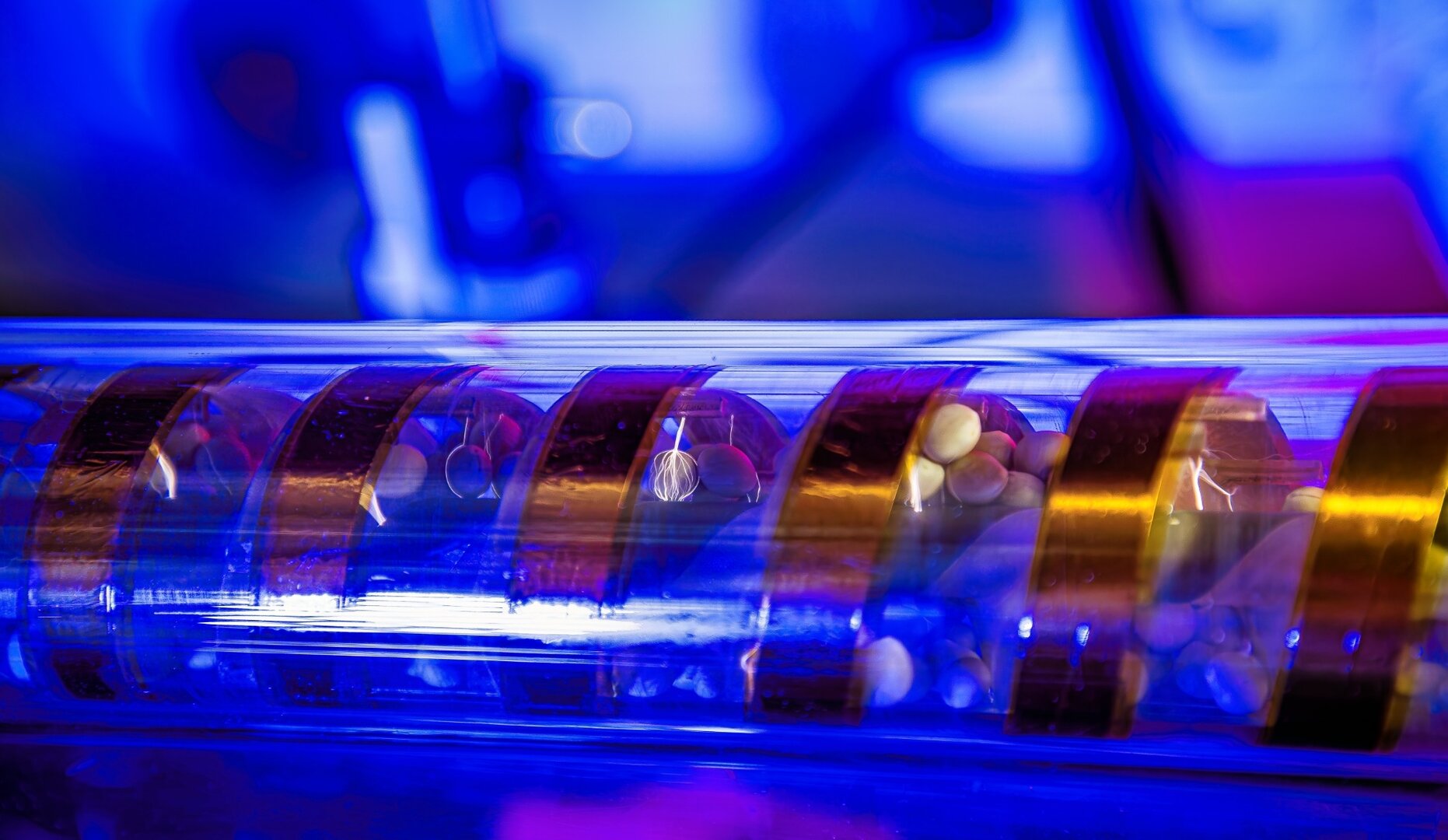 Saatgut in einer rotierenden Glasröhre während einer Plasmabehandlung, sichtbar durch blau-violette Entladungen zwischen den Elektroden.